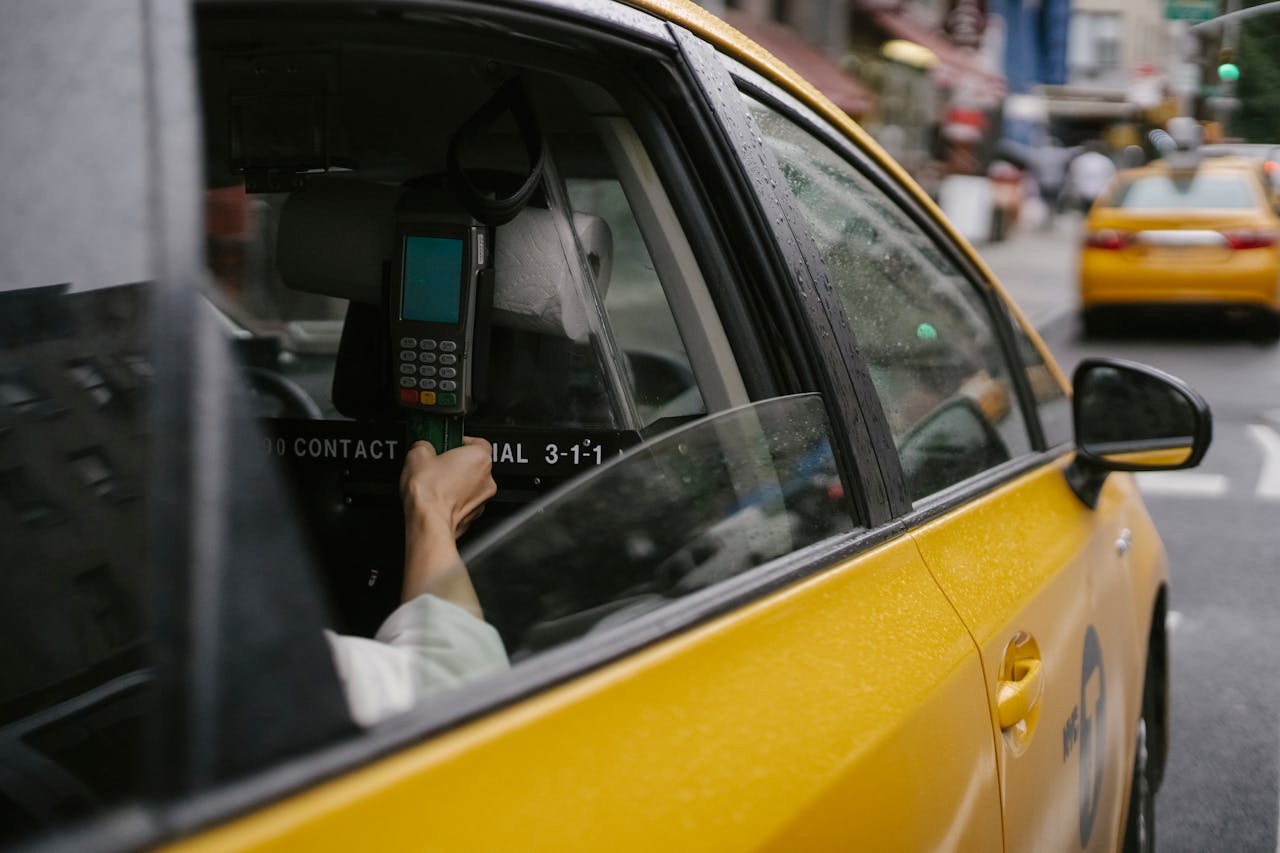 Unrecognizable passenger using credit card and payment terminal in yellow taxi car on road in town